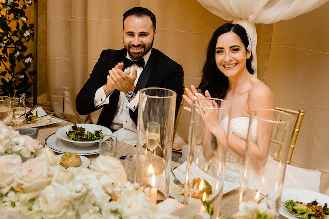 The bride and groom clapping at the dinner table. 