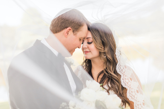 The bride and groom touching foreheads under the bride's veil.