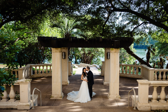 The groom kissing the bride's cheek under a pergola.