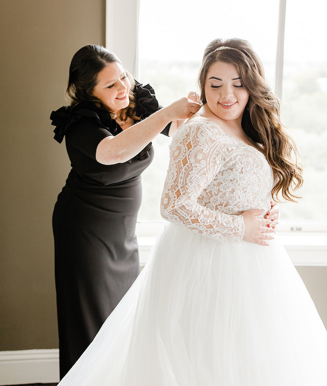 A bridesmaid helping button up the brides wedding dress.