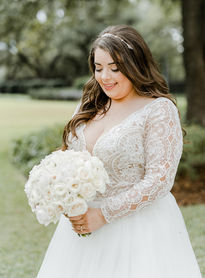 The bride wearing a lace wedding gown looking at her white rose bouquet. 