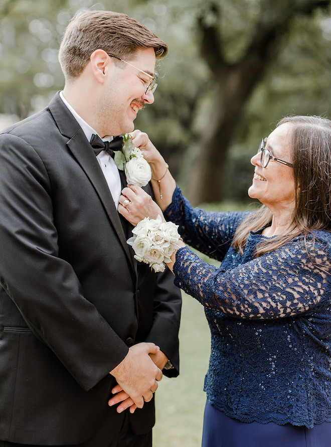 A woman in a blue lace dress pinning a flower on the grooms suit jacket. 