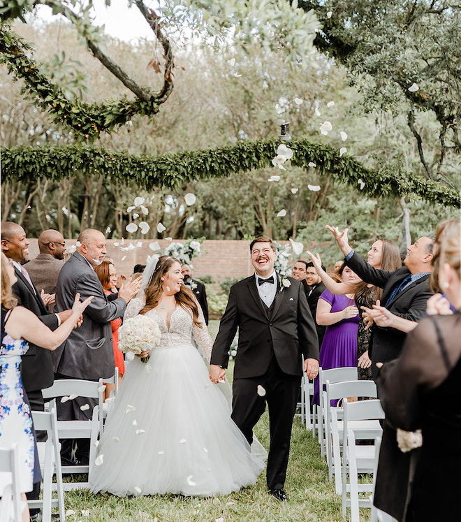 The bride and groom walking back down the aisle with the guests flowing white flower petals. 