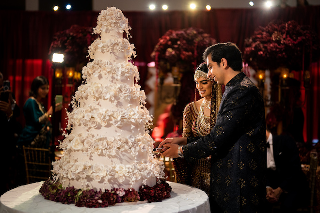 A bride and groom cutting a 7-tier white cake covered in white flowers.