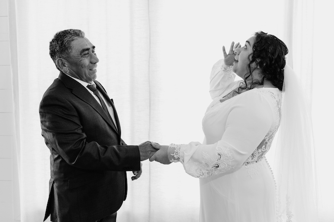 The bride wiping a tear and holding her father's hand.