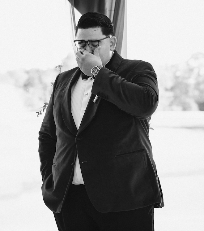 A black and white photo of the groom wiping tears at the altar. 