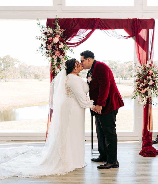 The bride and groom kissing in front of the red altar during their chapel ceremony.