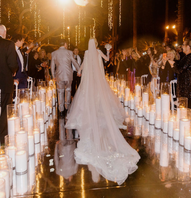 The bride and groom holding hands walking back down the aisle as guests on either side of them clap and take pictures.