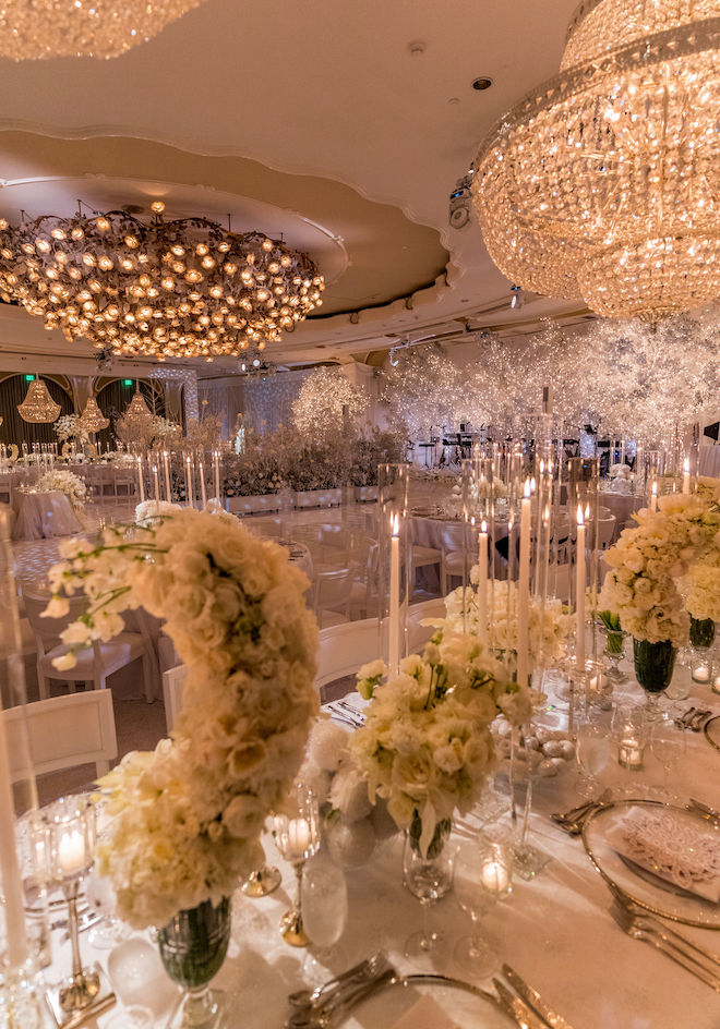 White florals, pillar candles and grand chandeliers decorating the reception space.