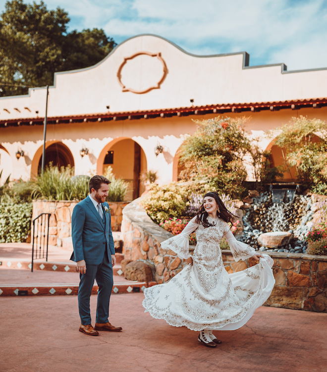 The bride twirling in her ivory and gold gown during the first look with the groom in front of Madera Estates. 