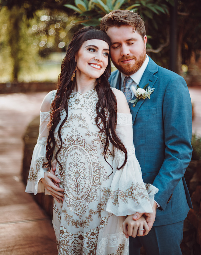 The bride smiling and holding the groom's hand. The groom is behind her and closing his eyes and smiling. 