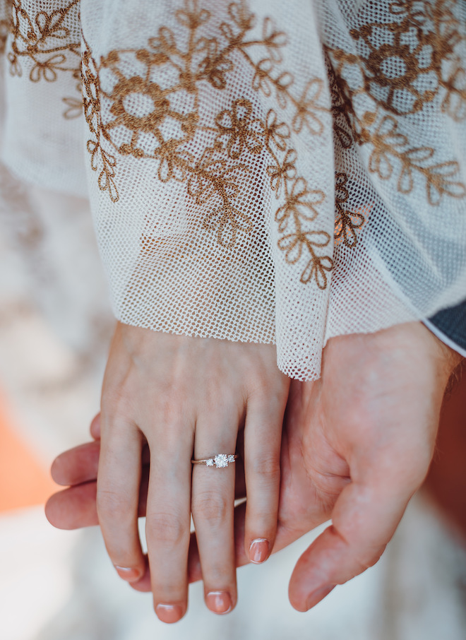 The bride and groom holding hands showing the bride's gold engagement ring with three diamonds. 