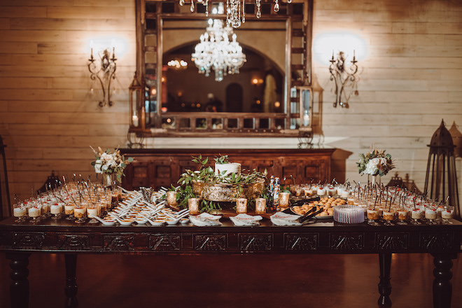 A table full of different deserts with a white cake in the middle surrounded by greenery.