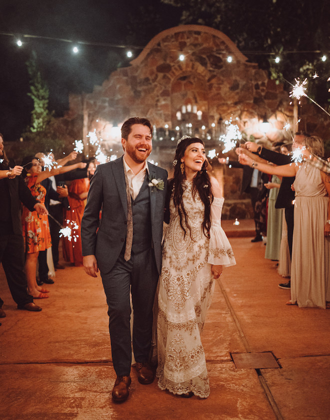 The bride and groom walking back down the aisle while guests wave sparklers on either side of them. 