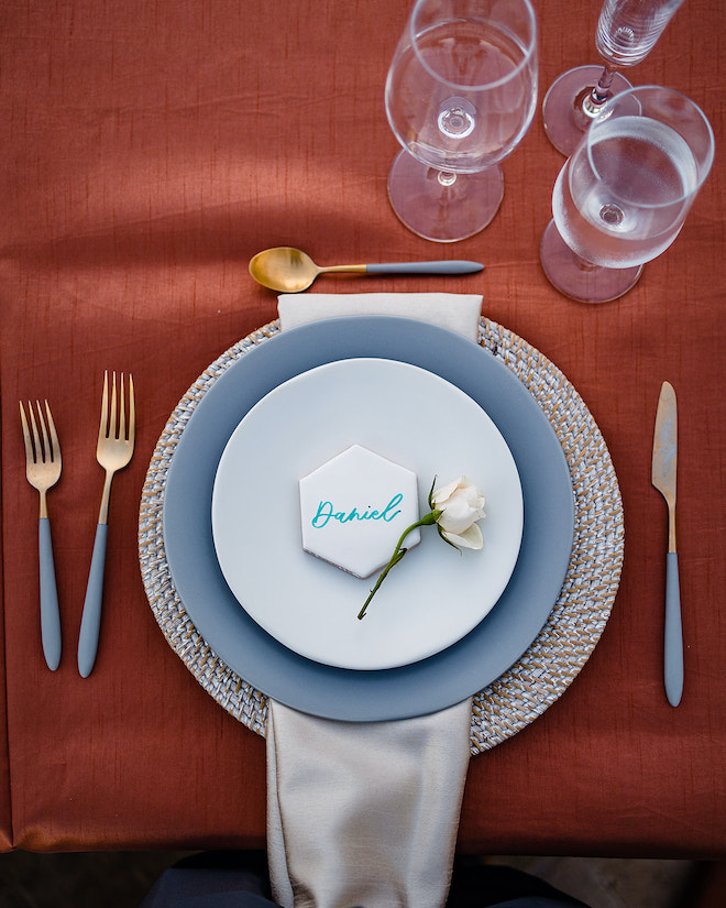 White and blue plates and flatware sitting on a burnt orange tablecloth. 