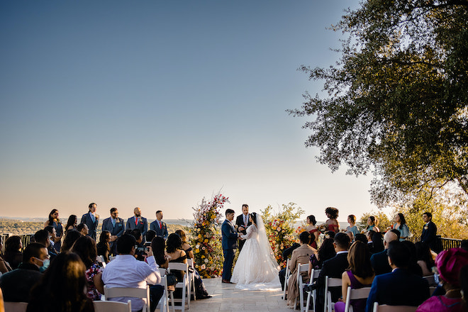 A bride and groom holding hands at the altar while guests watch them during their alfresco autumn ceremony. 