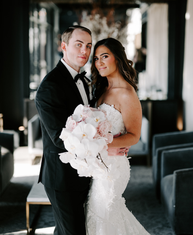 The bride and groom smiling while the bride holds a bouquet with orchids and pink roses. 