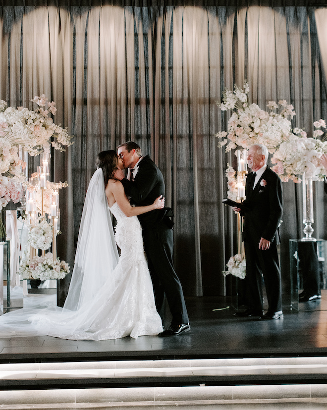 The bride and groom kissing at the altar decorated with white and blush floral arrangements. 