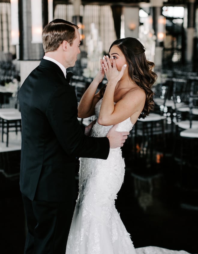 The groom hugging the bride's waist as she wipes tears from her eyes. 