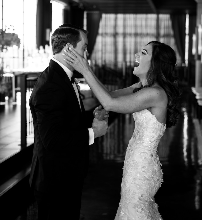 The bride smiling and wiping tears from the groom's face during their first look. 