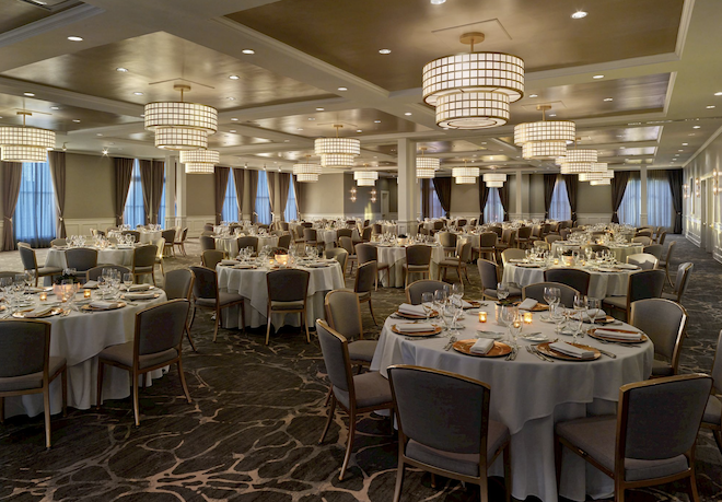 A ballroom with round tables decorated with blue linens and gold plates.