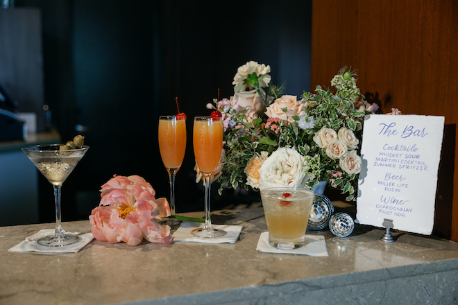 The bar at The Westin Houston Memorial City with a white cocktail menu with blue writing and four cocktails with flowers and disco balls around them.