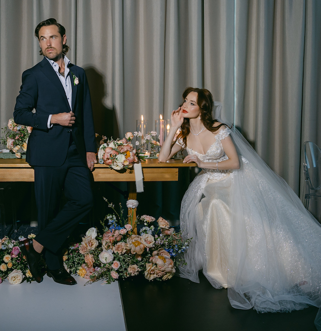 The bride sitting at the reception table looking at the groom. The reception table is covered in florals and candles. 