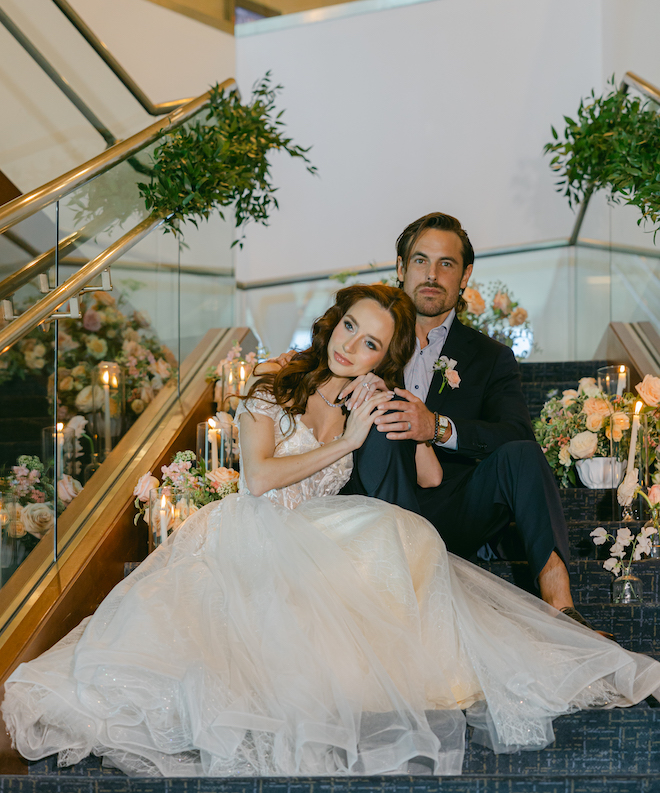 The bride resting her head on the groom while sitting on the staircase at The Westin Houston Memorial City covered in florals and candles. 