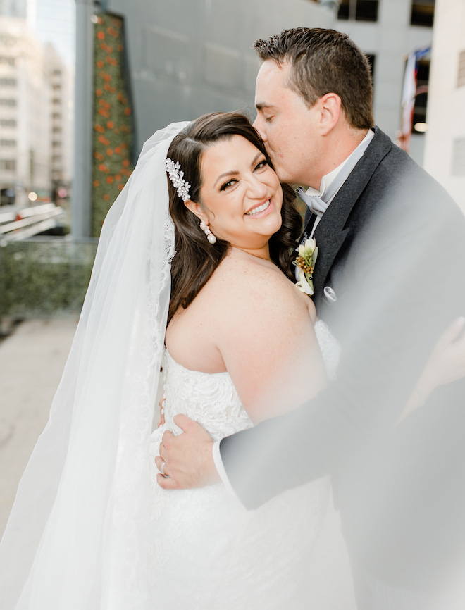 The groom kissing the side of the brides head as they are hugging.