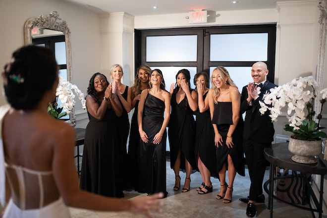 The wedding party wearing black reacting to seeing the bride in her wedding gown. 