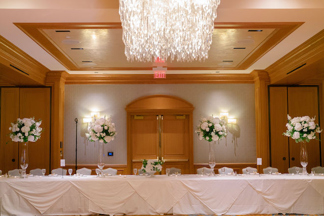 A simple, yet sophisticated ballroom reception decorated in tall white floral arrangements and white linens at St. Regis Houston. 