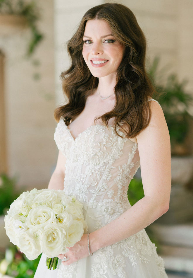 The bride poses in her lace Galia Lahav wedding gown while holding her wedding bouquet of roses. 