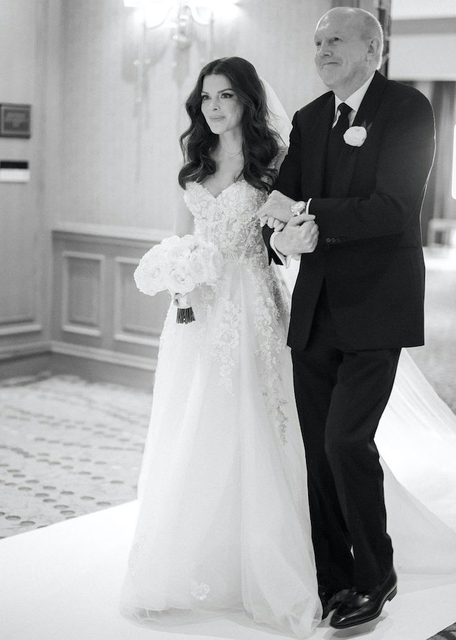 The bride is escorted down the aisle on her wedding day by her father. 