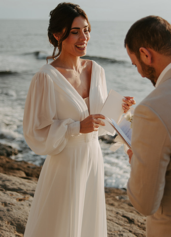 The bride smiling while the groom reads his vows. 