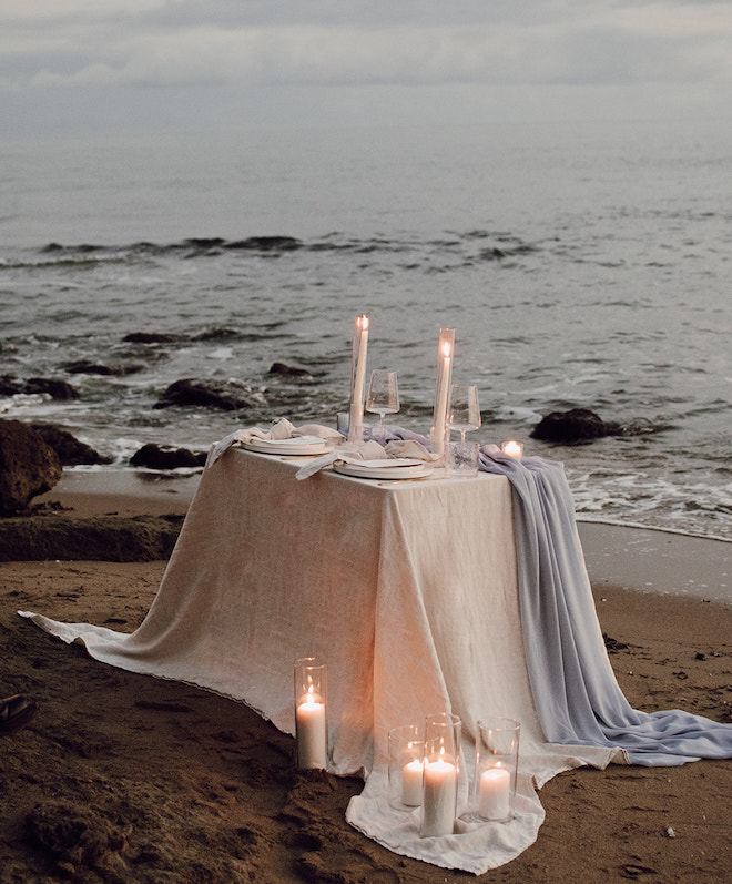 A table with cream and blue linens and candleliight on the beach for an intimate elopement.