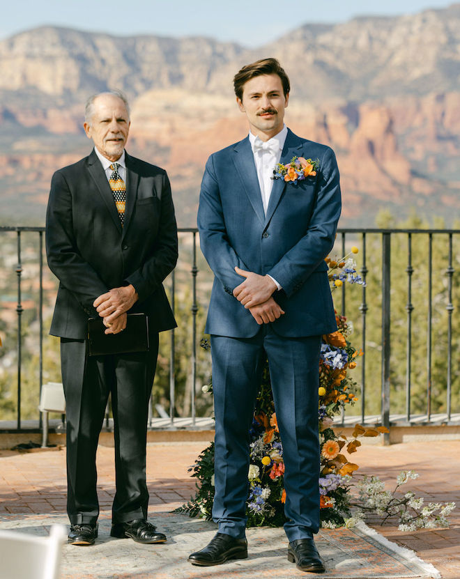 The groom and officiant standing at altar looking down the aisle. 