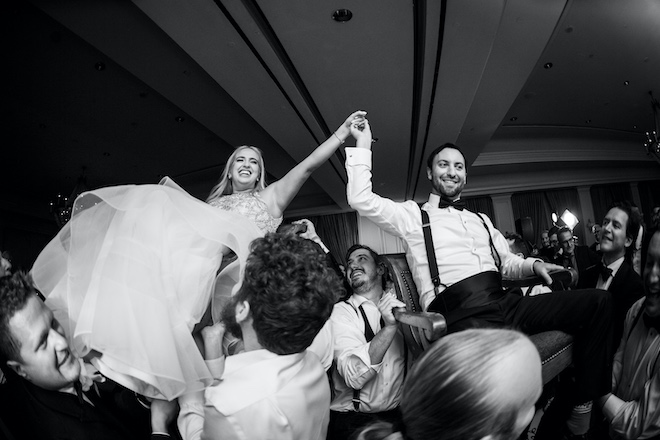 The bride and groom holding hands while being lifted in their chairs during the reception.