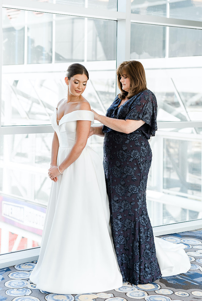 The bride's mother helps her daughter zip up her white wedding gown. 