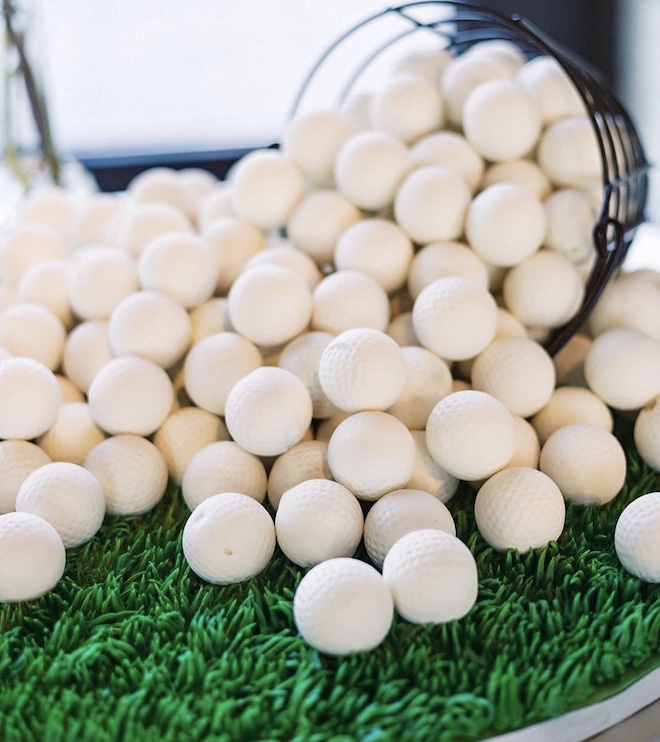 Cake balls made to look like golf balls spilling on grass made out of icing.