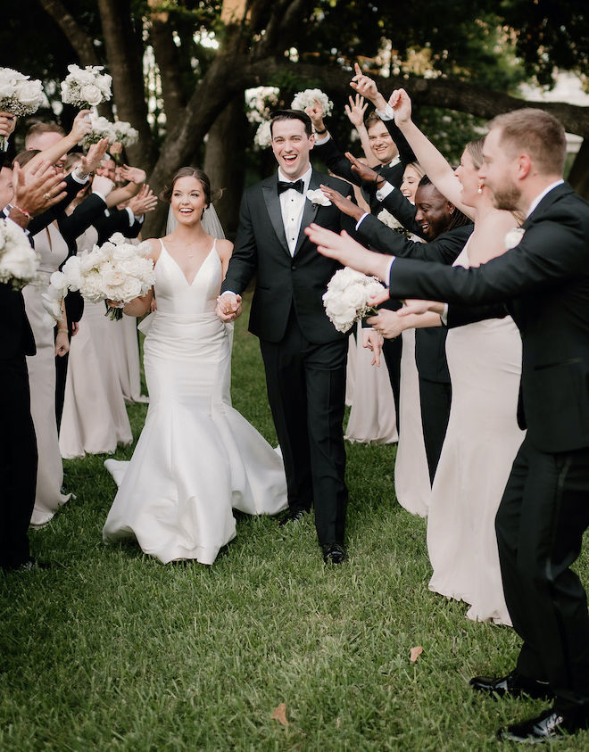 The bride and groom holding hands walking through the wedding party. 