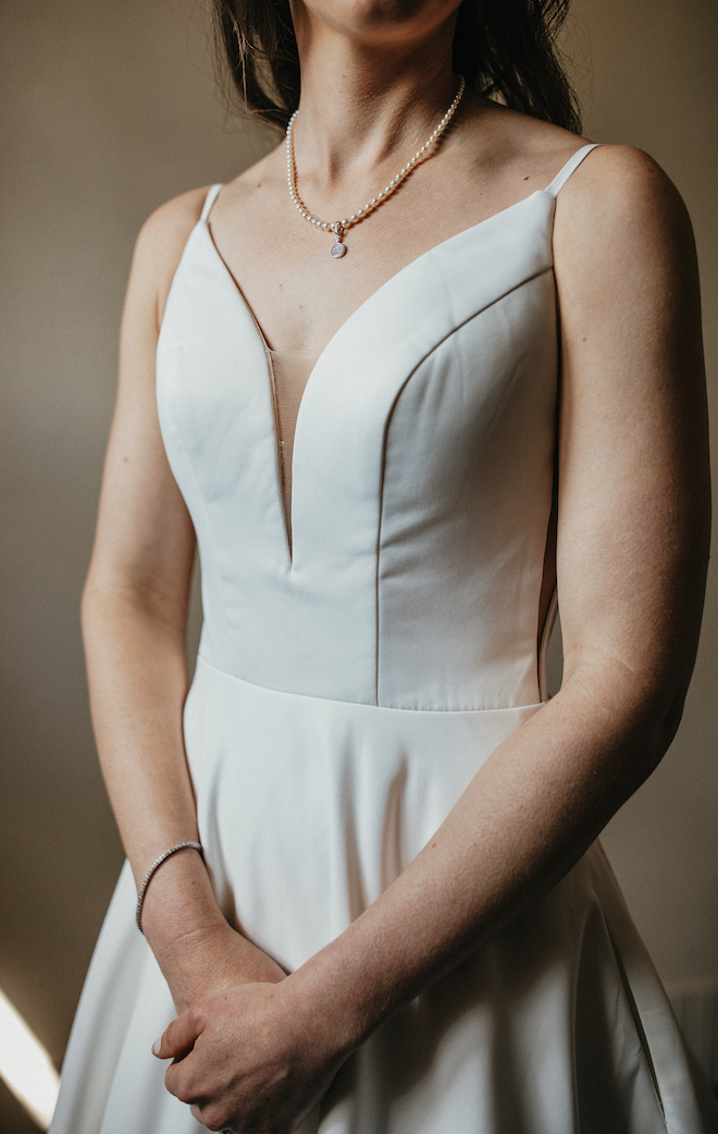 The bride poses holding her hands at her waist wearing her white wedding down, silver diamond bracelet and pearl necklace. 