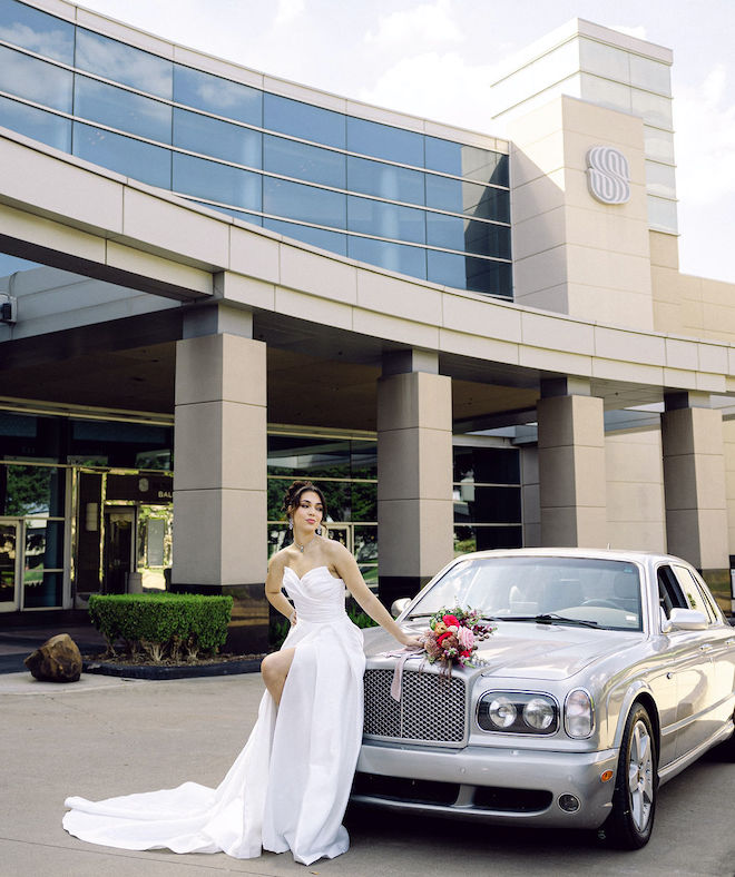 The bride poses beside a vintage car outside the hotel wedding venue, the Royal Sonesta Houston Galleria.