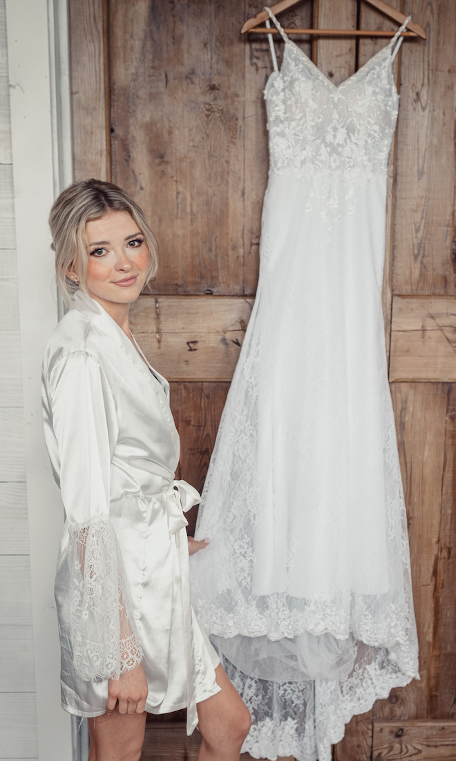 The bride smiles next to her dress in the bridal suit at the Chapell Hill wedding venue, Hummingbird Hill. 