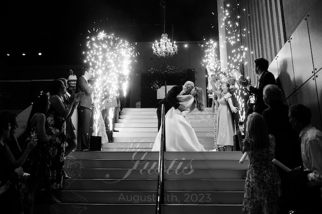 The bride and groom kissing on the stairs at The Ballroom at Bayou Place with sparkers on either side of them.