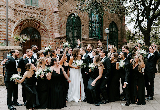 The bride and groom share a kiss outside of their wedding ceremony as their wedding party celebrates around them.