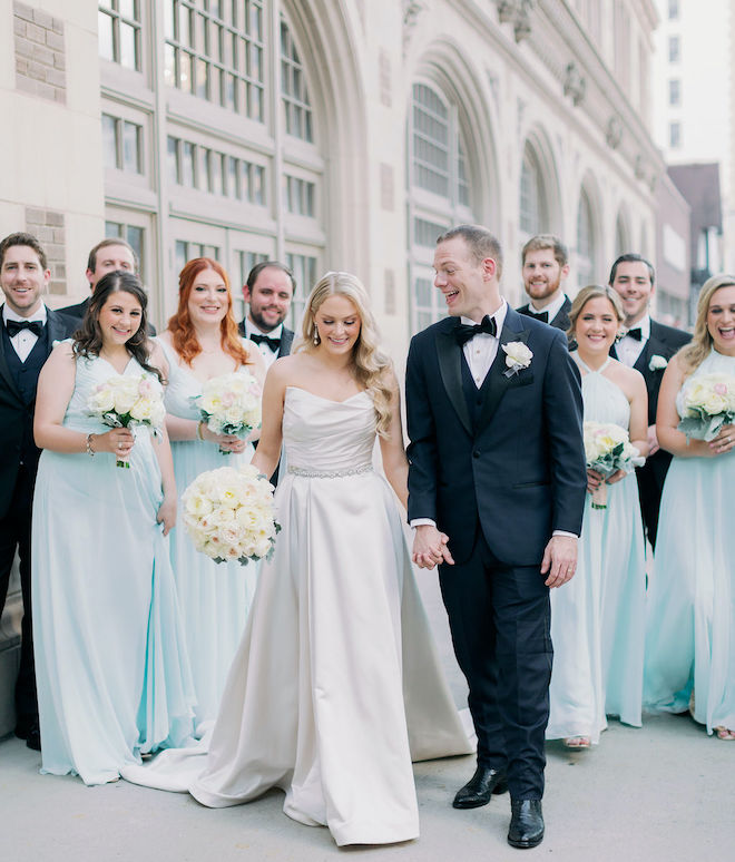 The bride and groom holding hands with the wedding party behind them.