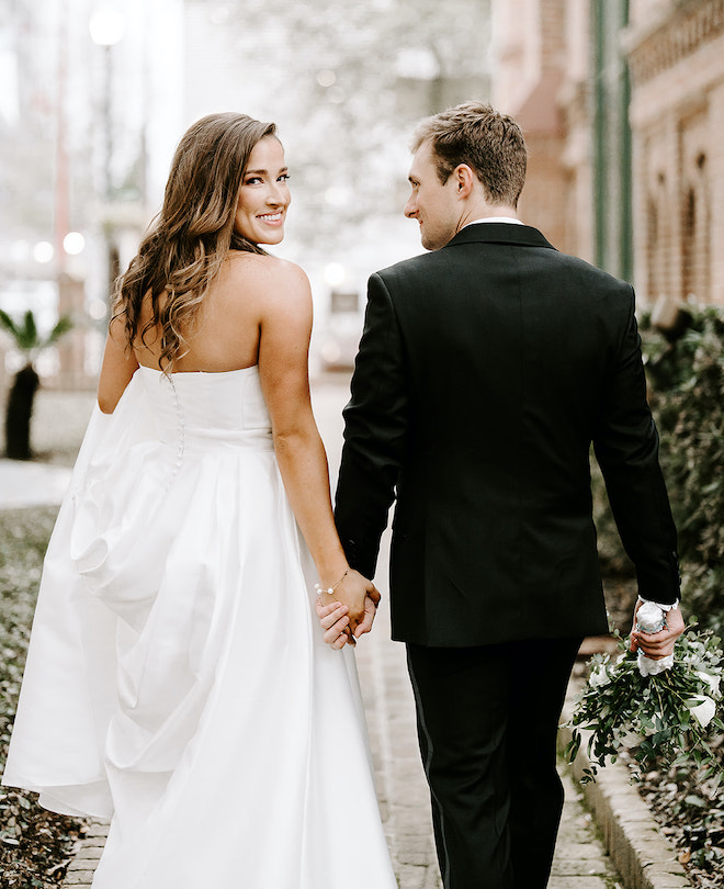 The bride and groom hold hands and look over their shoulders outside of a Houston church in the city. 