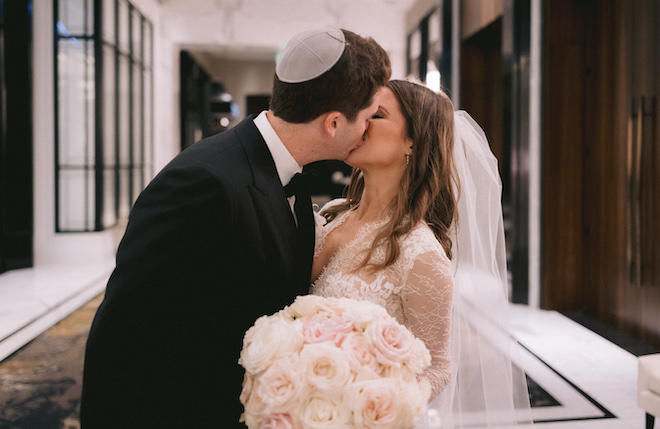 The bride and groom shar a kiss in the atrium of their wedding venue, The Post Oak Hotel at Uptown. 