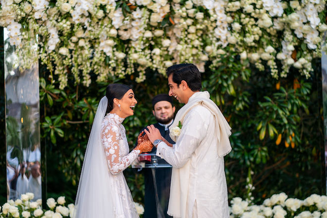 The bride and groom exchange vows under white flowers by The Events Company.