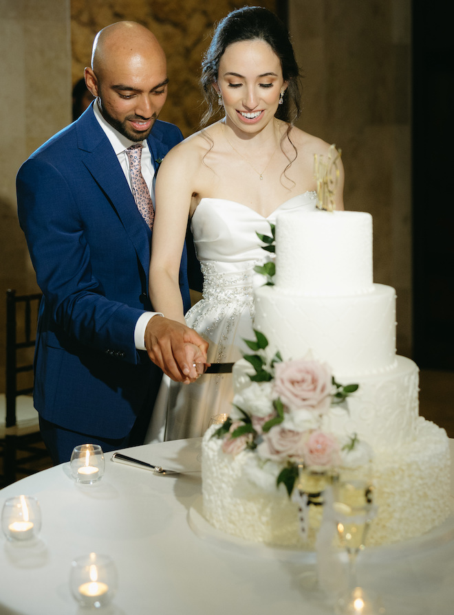 The bride and groom slice into their four-tier white wedding cake.